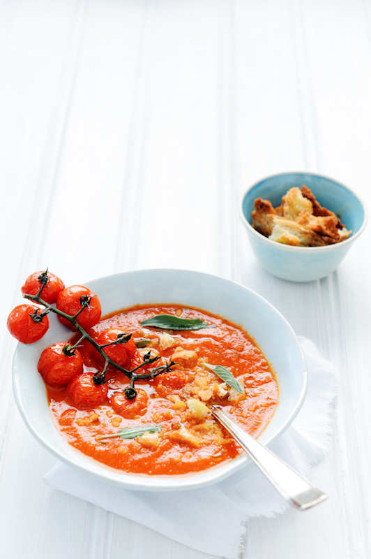 Bowl of fresh delicious tomato soup with croutons and sage garnish on white rustic surface; healthy eating